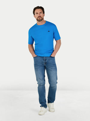 Man wearing a blue t-shirt and jeans standing against a white background