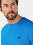 Man wearing a blue shirt with a small logo on a light gray background