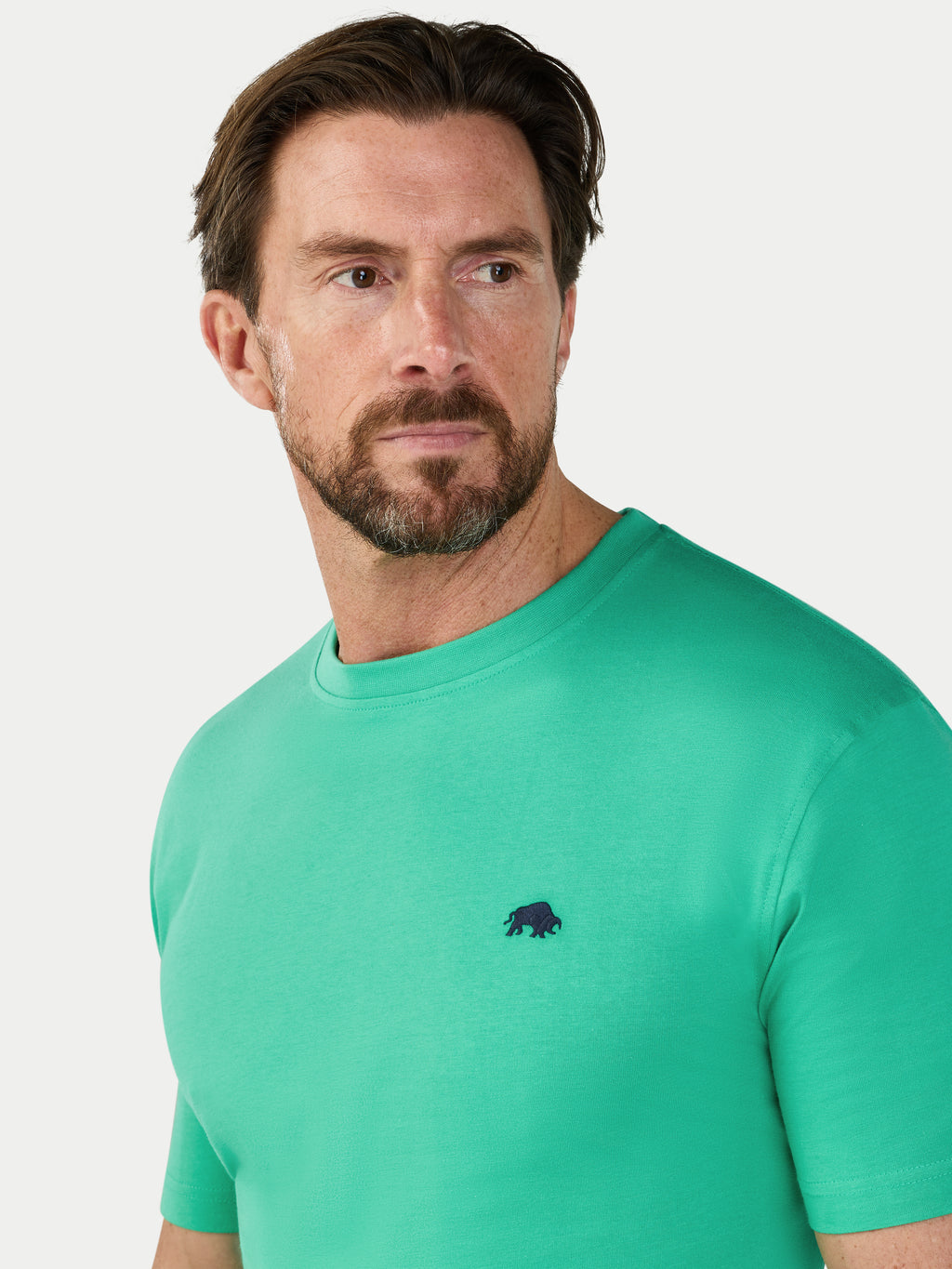 Man wearing a green t-shirt with a small black logo on a light gray background