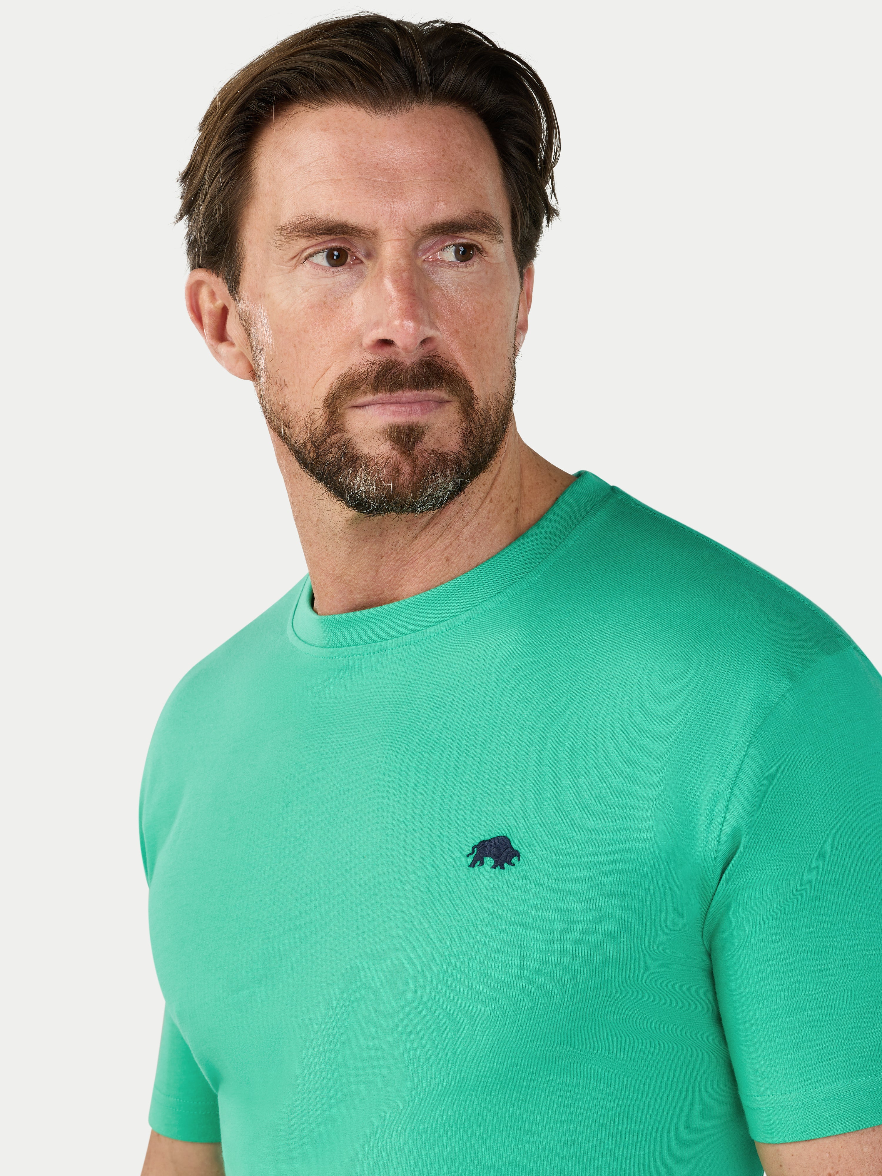 Man wearing a green t-shirt with a small black logo on a light gray background