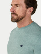 Man wearing a green t-shirt with a small logo on a light gray background