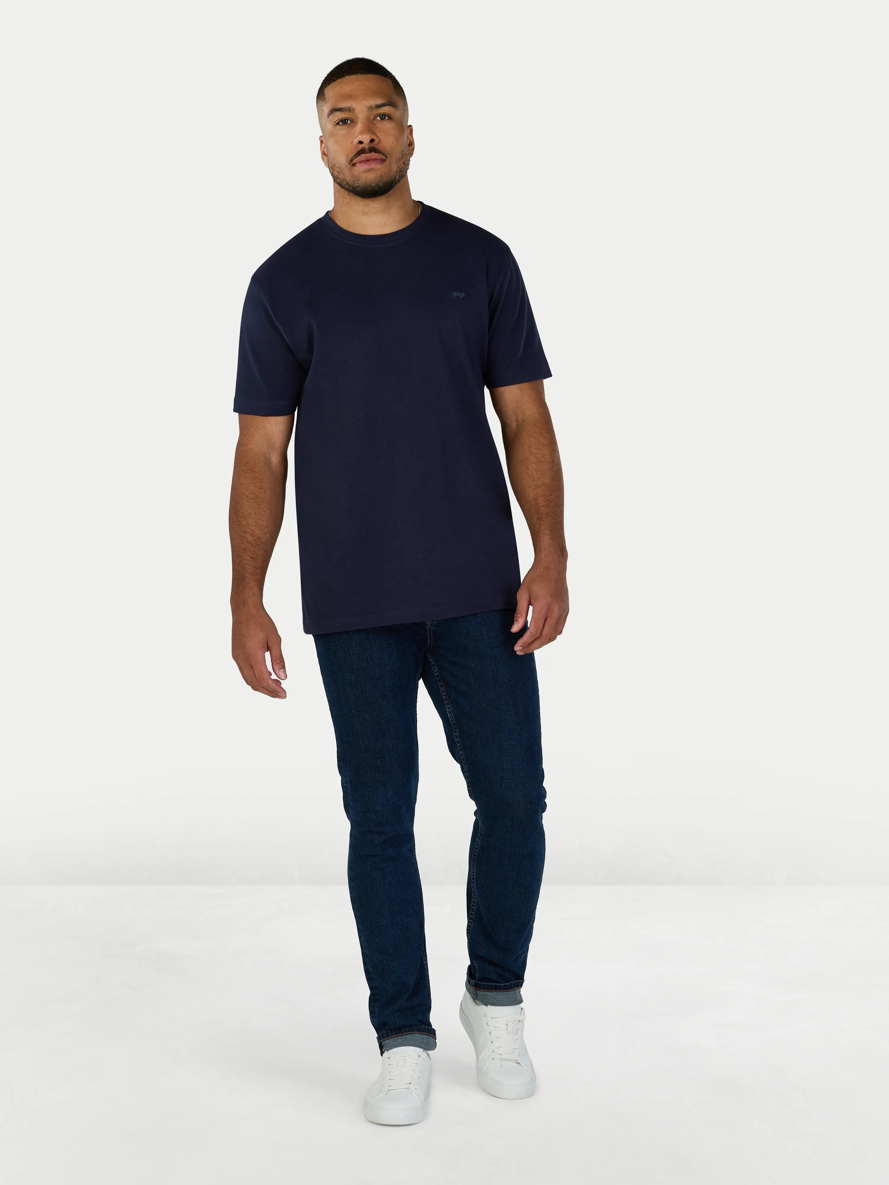 Man wearing a navy t-shirt and jeans on a white background