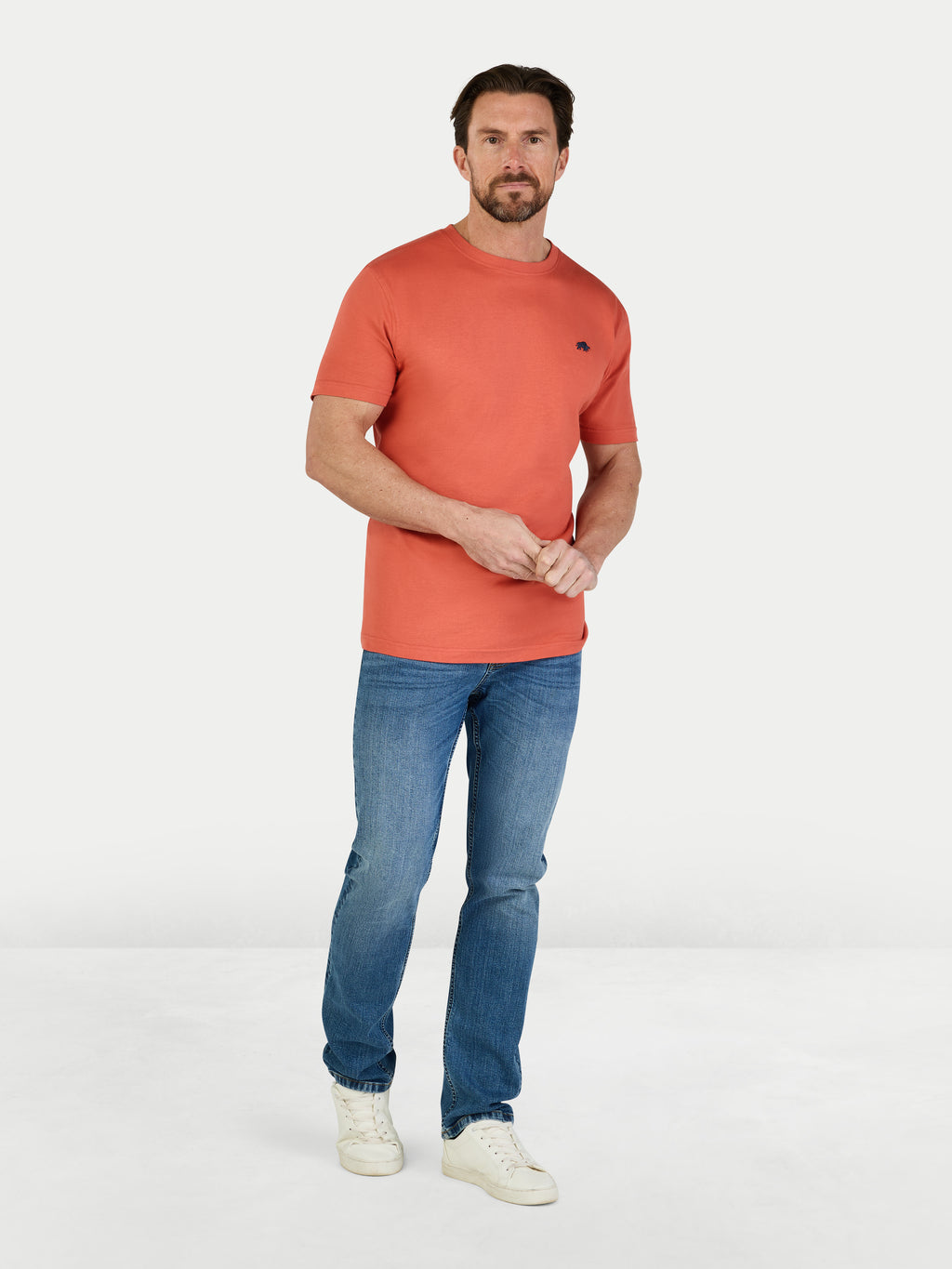 Man wearing an orange t-shirt and blue jeans on a white background