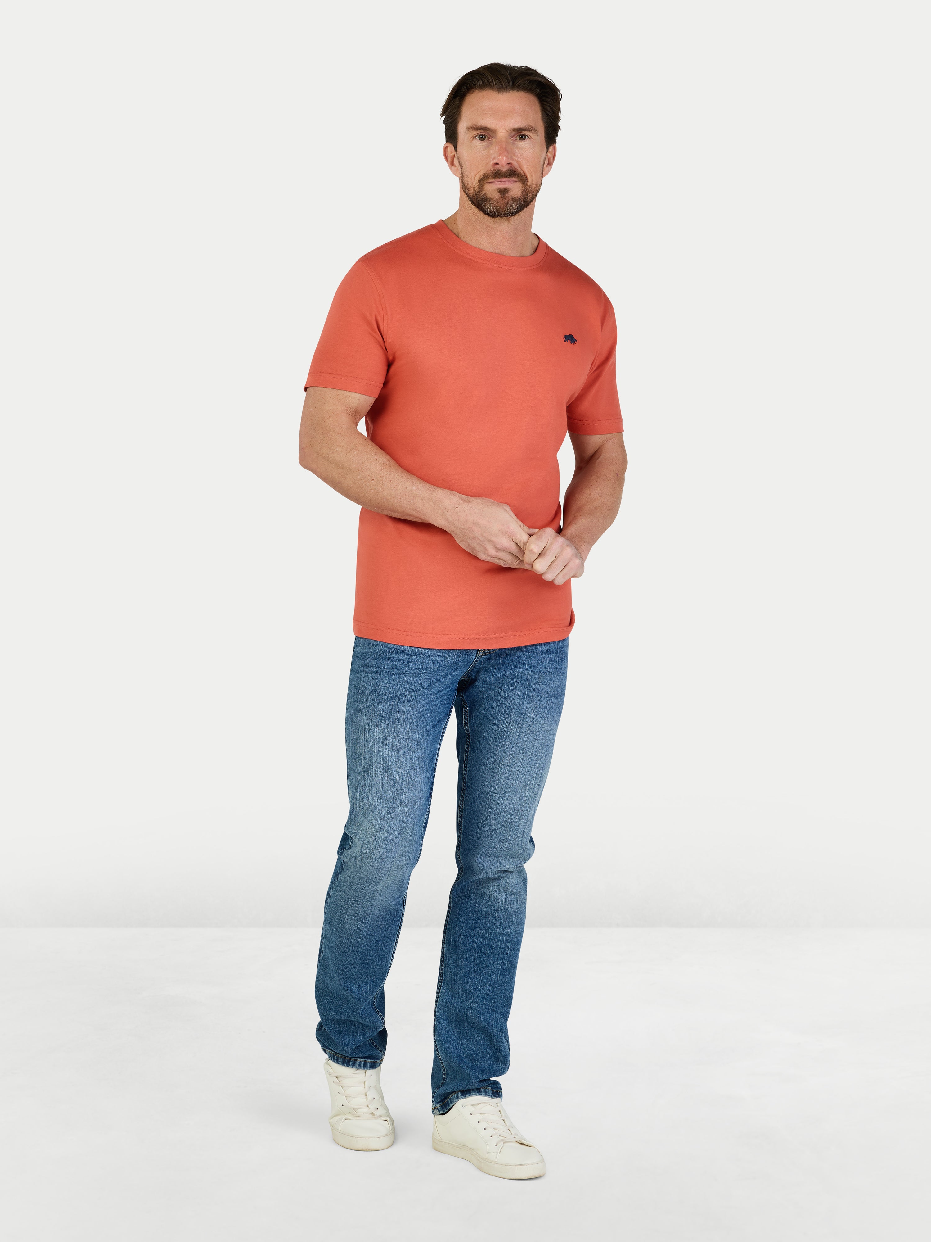 Man wearing an orange t-shirt and blue jeans on a white background