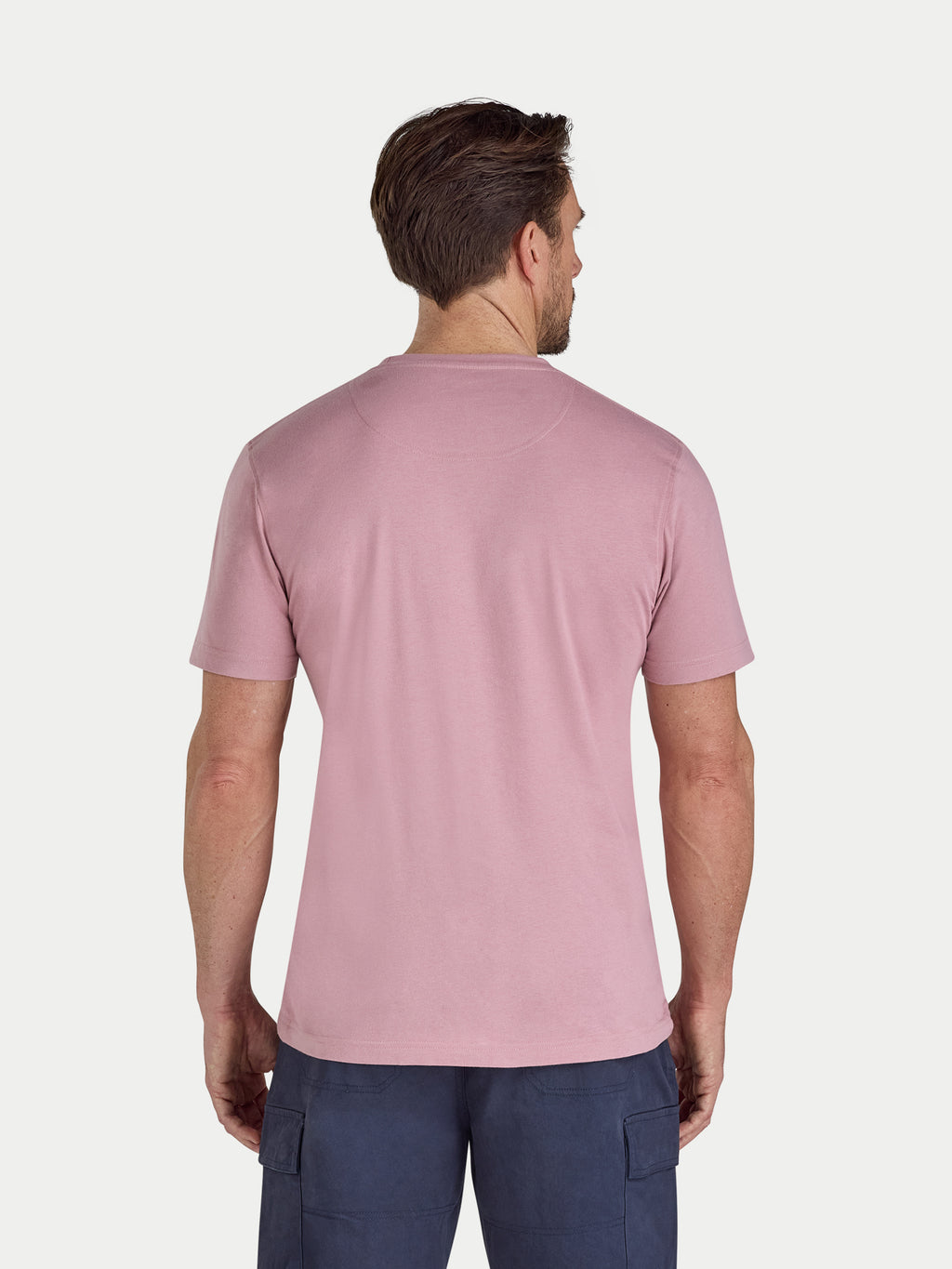 Man wearing a pink t-shirt and navy pants on a white background