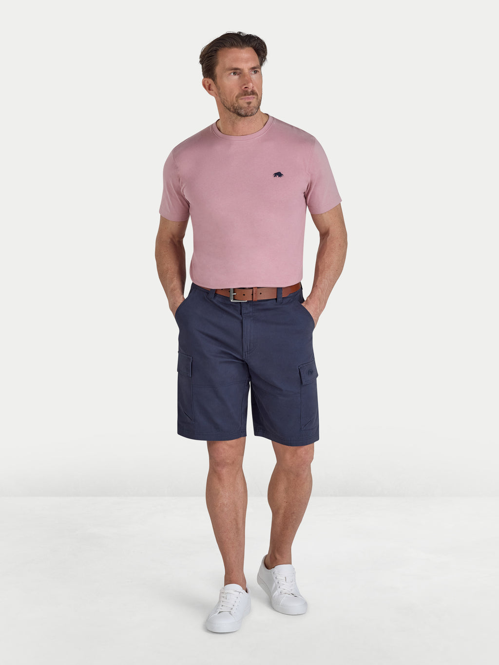 Man wearing a pink t-shirt and navy cargo shorts on a white background