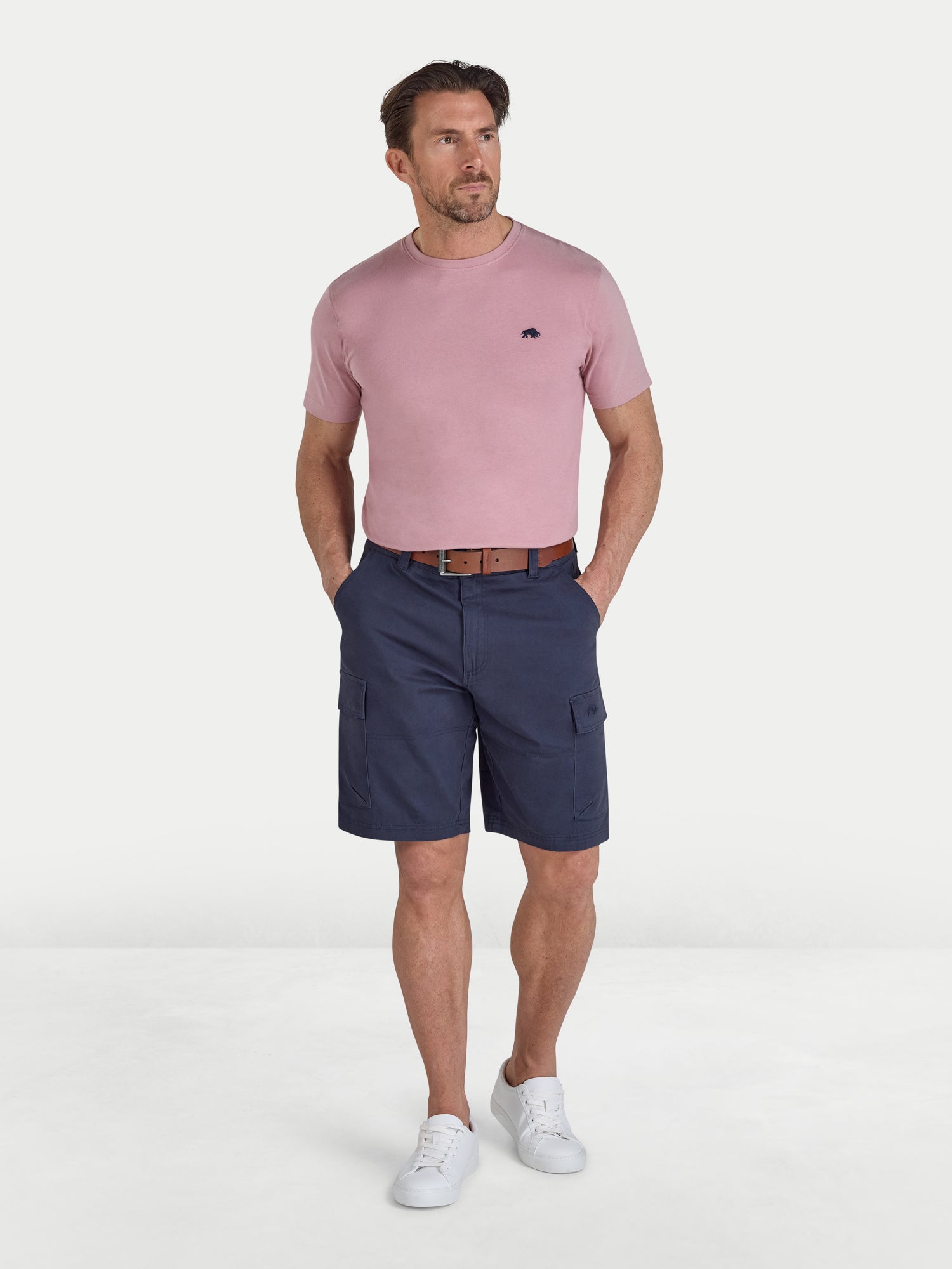 Man wearing a pink t-shirt and navy cargo shorts on a white background
