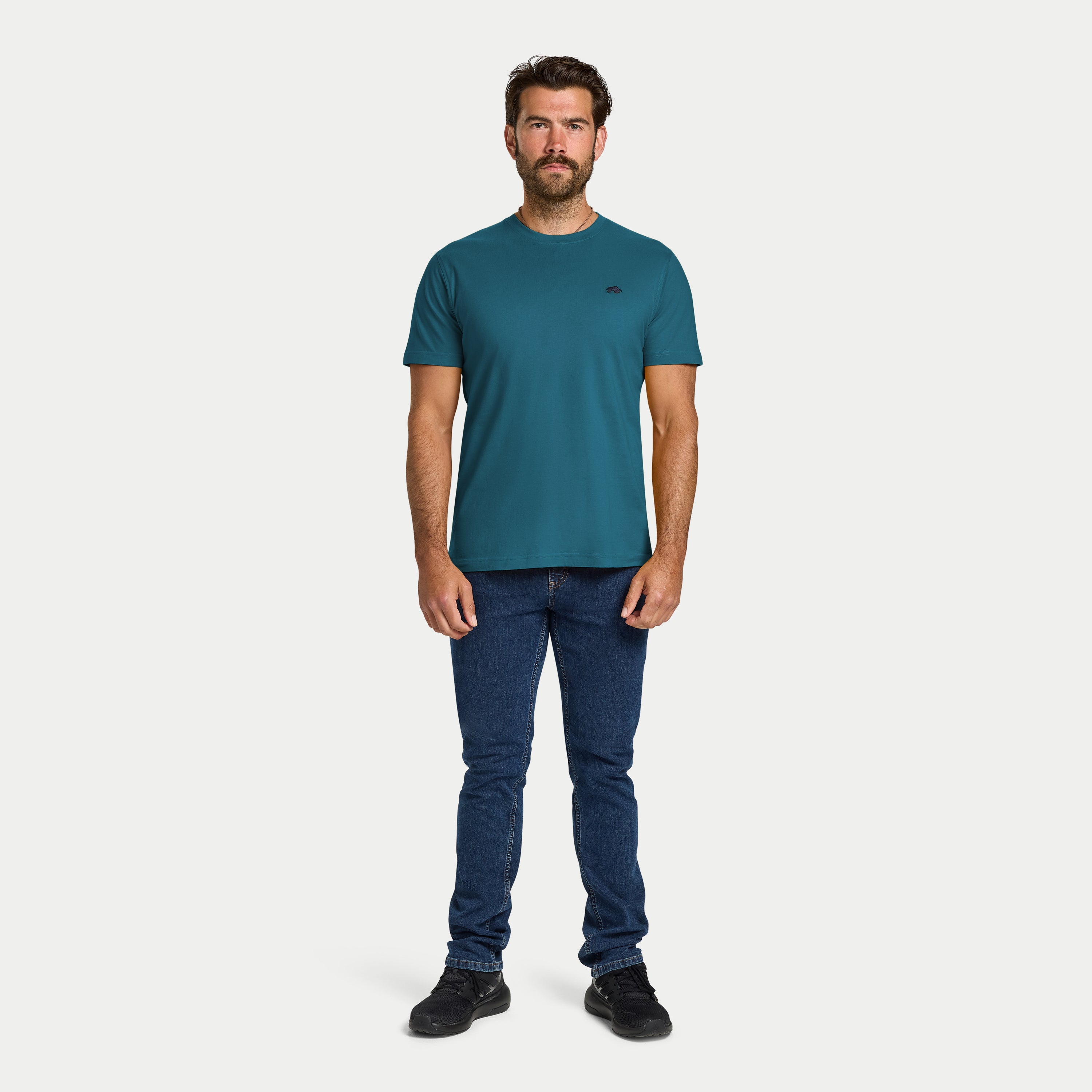 Man wearing a teal t-shirt and blue jeans on a white background