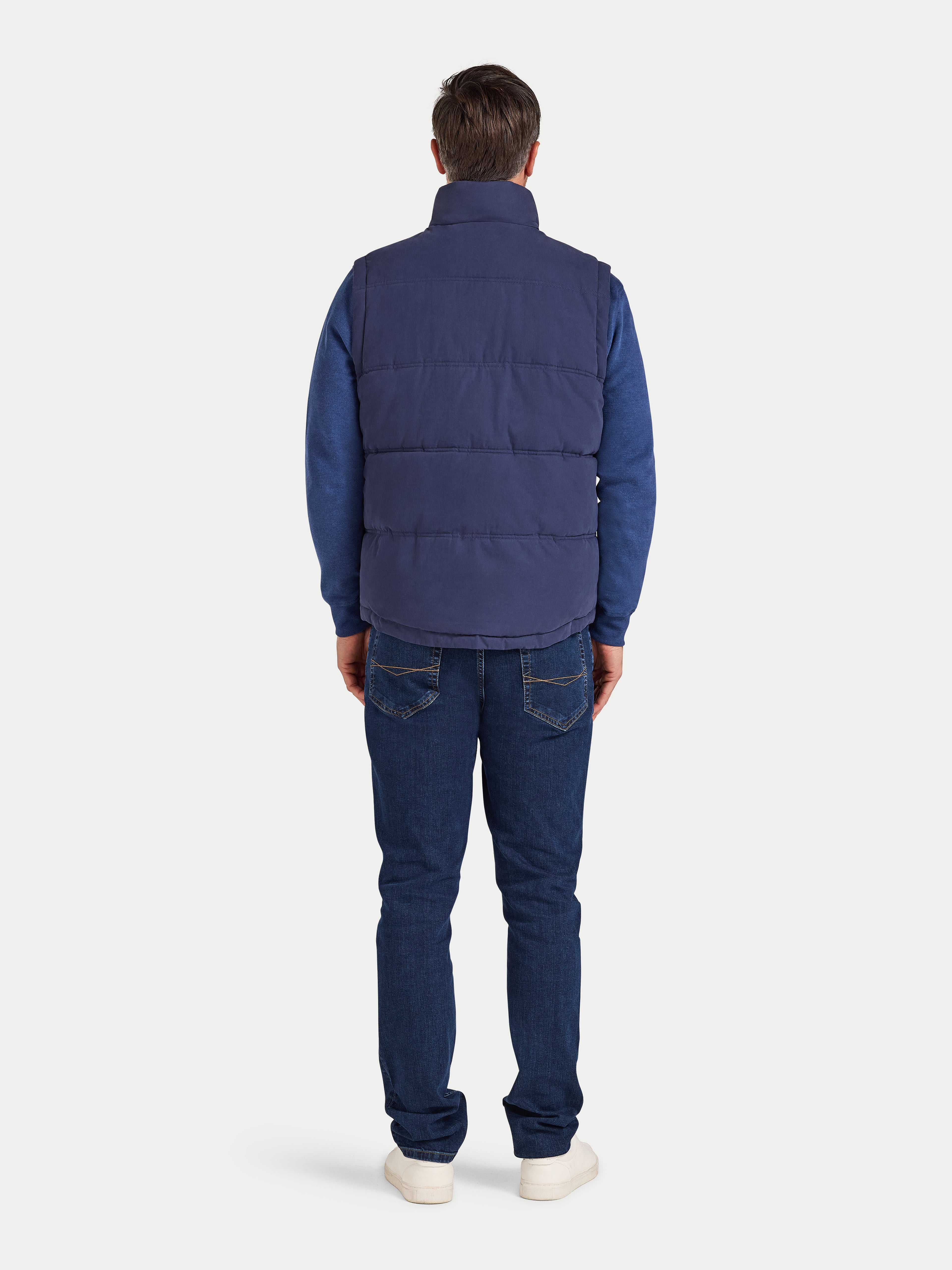 Person wearing a blue puffer vest and jeans on a white background
