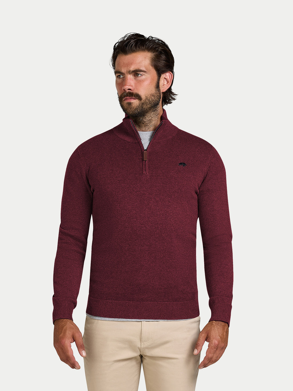 Man wearing a burgundy sweater with a logo on a light gray background