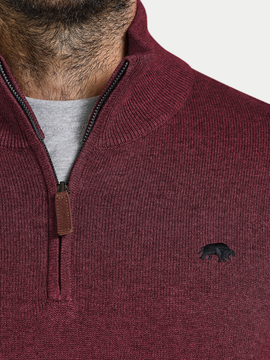 Close-up of a maroon sweater with a logo on a white background