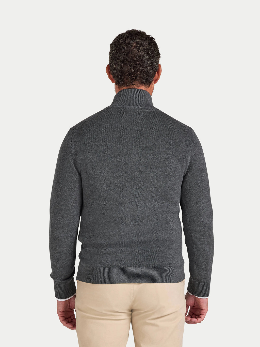 Man wearing a gray sweater and beige pants on a light gray background