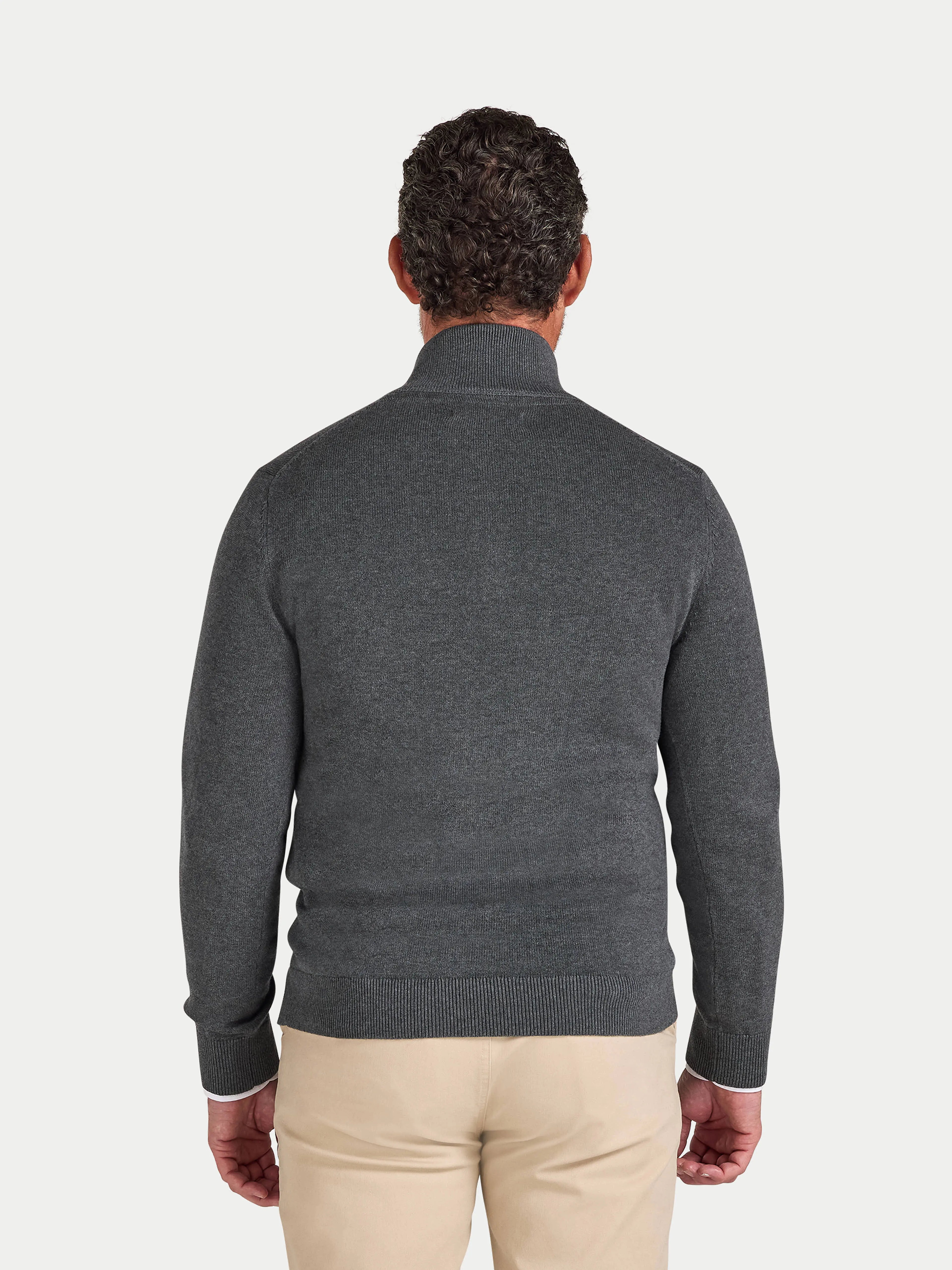 Man wearing a gray sweater and beige pants on a light gray background