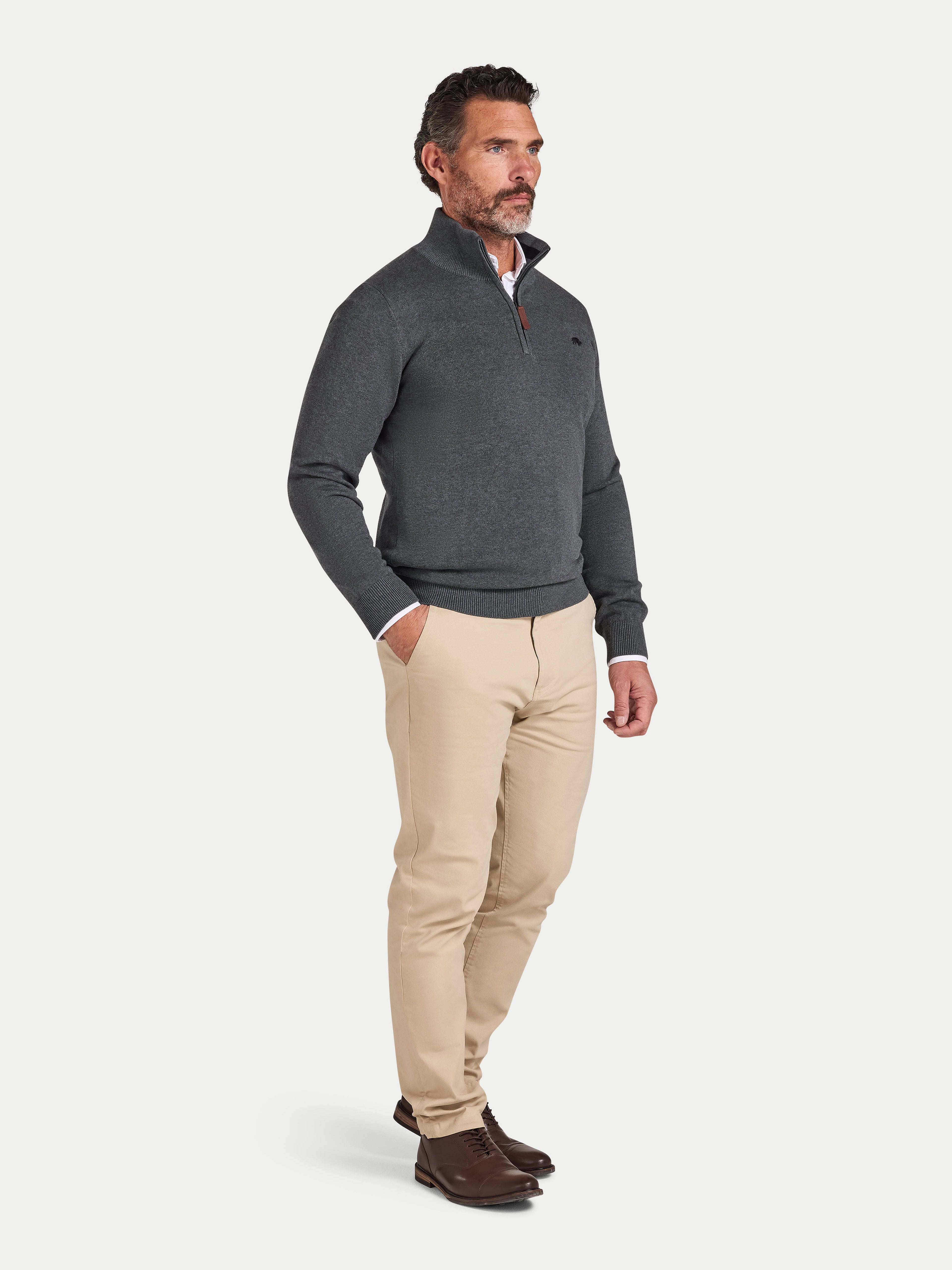 Man wearing a gray sweater and beige pants on a white background