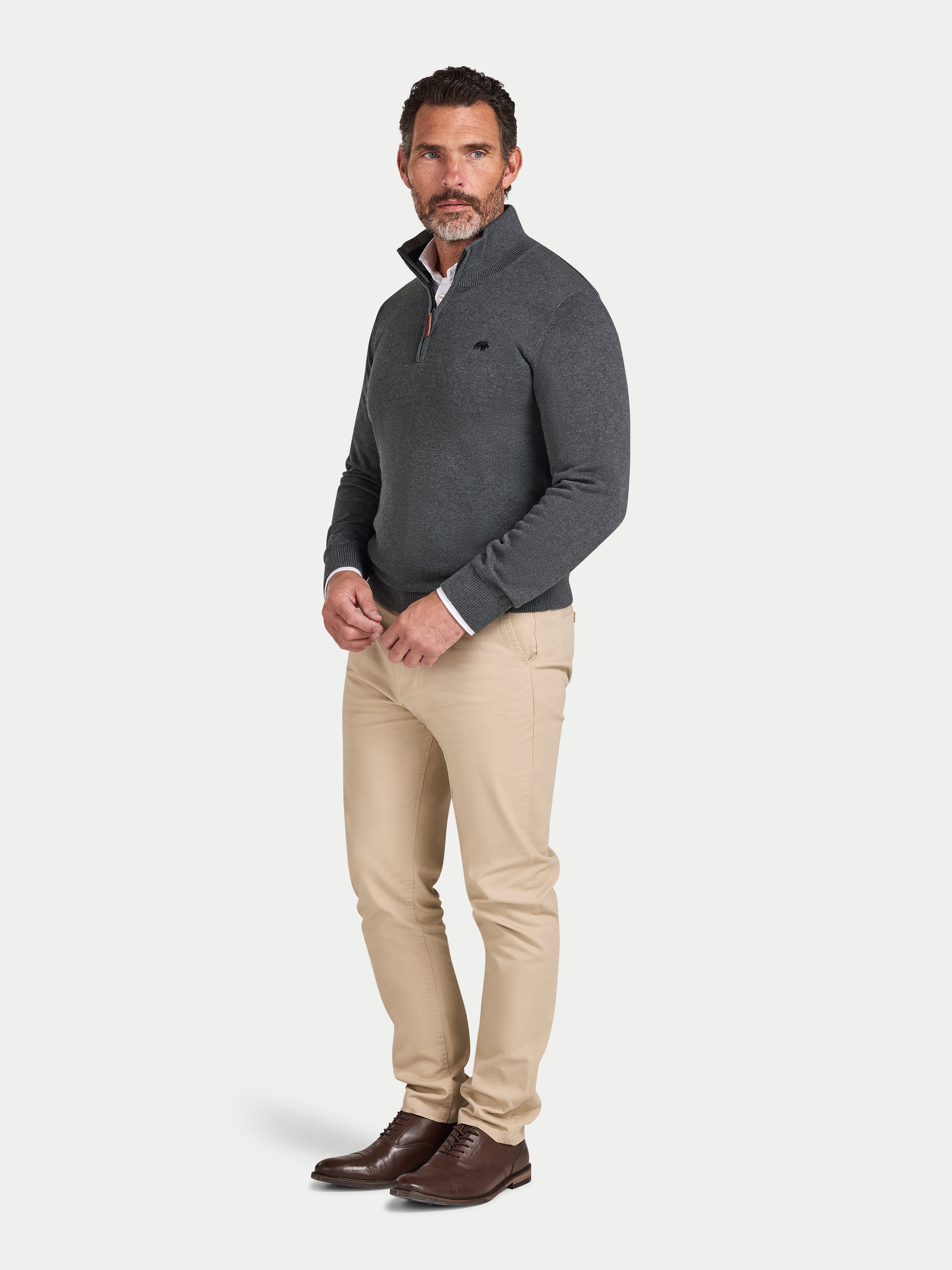 Man wearing a gray sweater, beige pants, and brown shoes on a white background