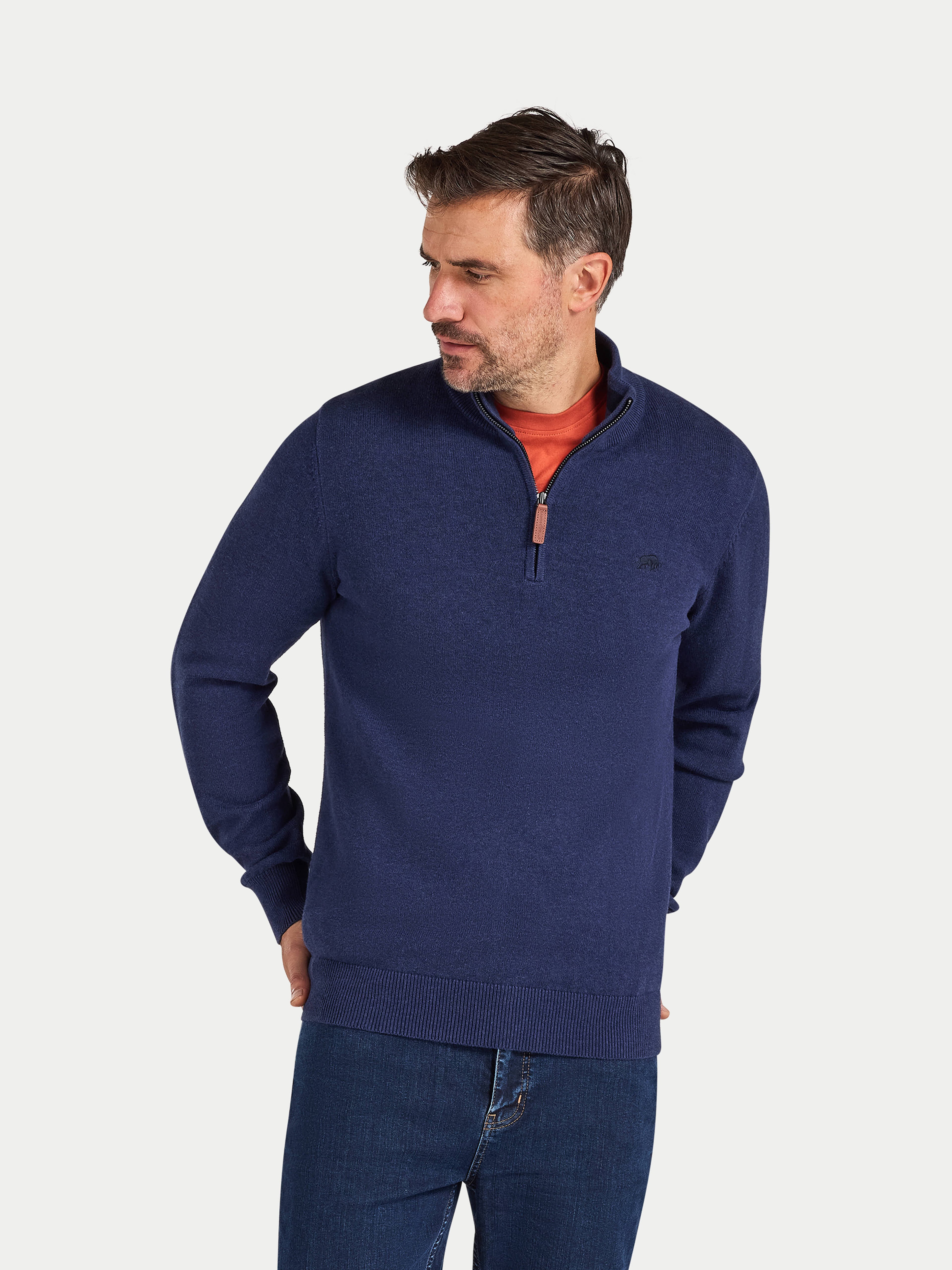 Man wearing a navy blue pullover with a red shirt underneath on a light gray background