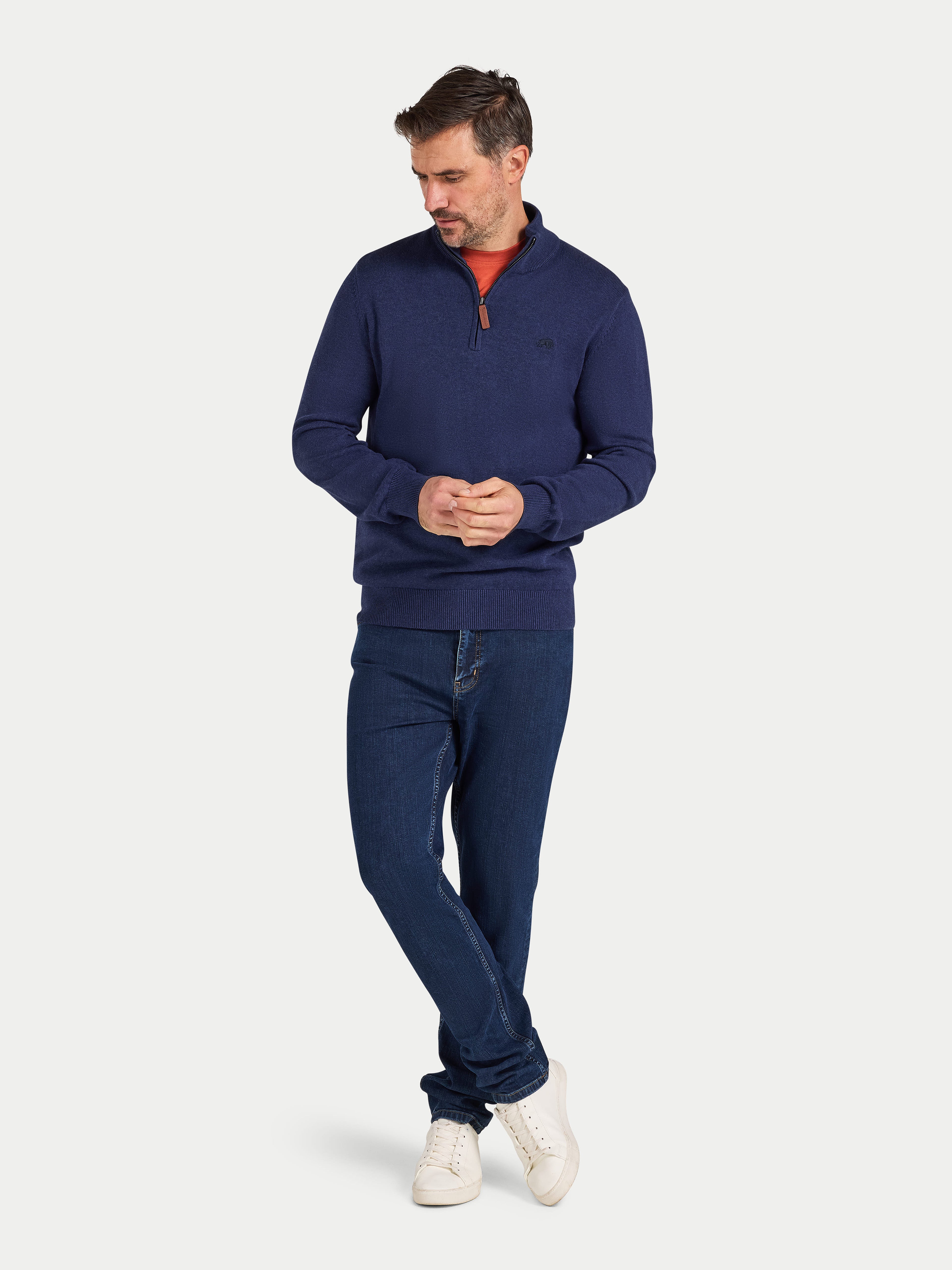Man wearing a navy sweater and jeans on a white background
