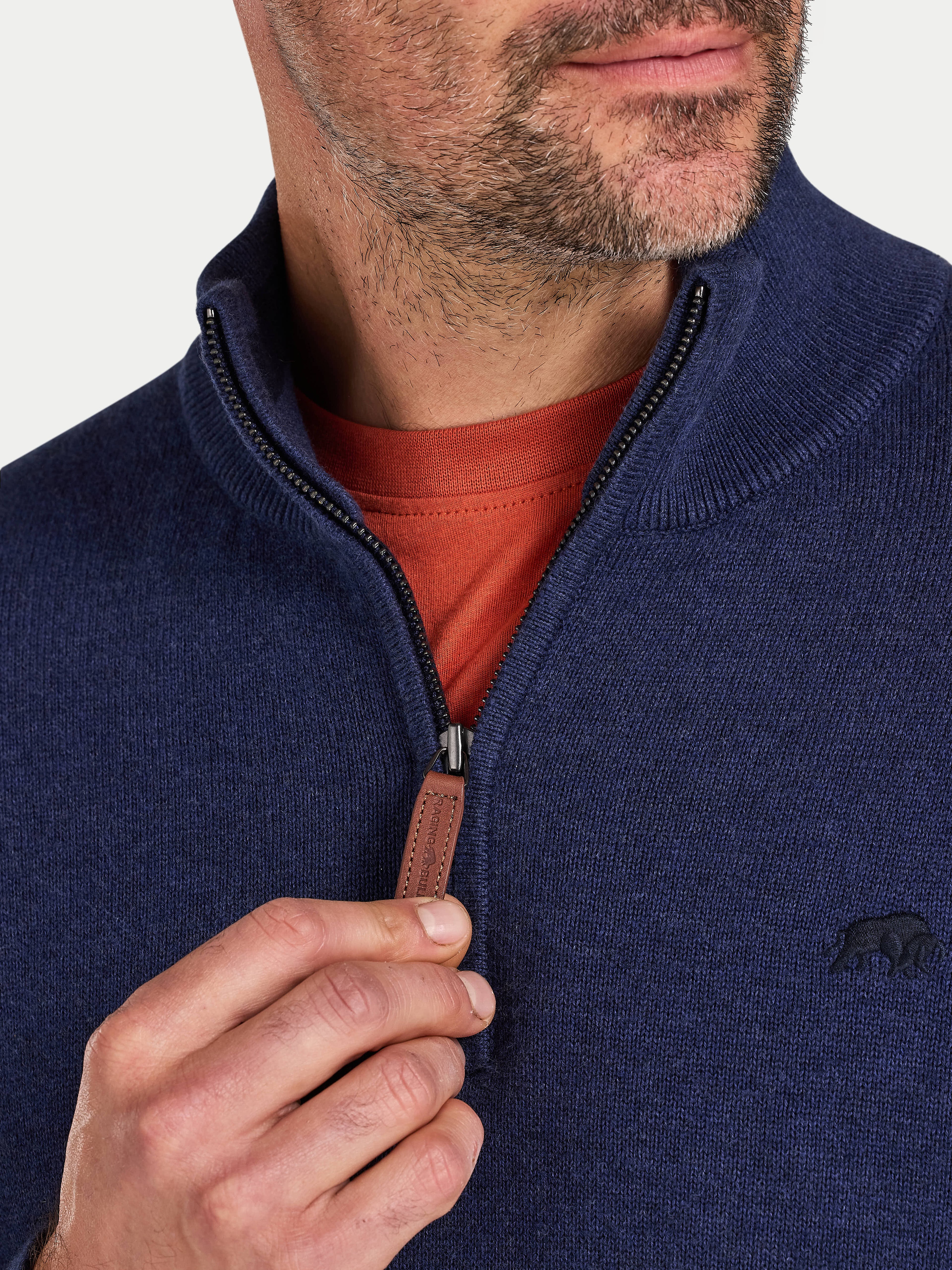 Man wearing a navy blue zip-up sweater over a red shirt with a visible brand logo.