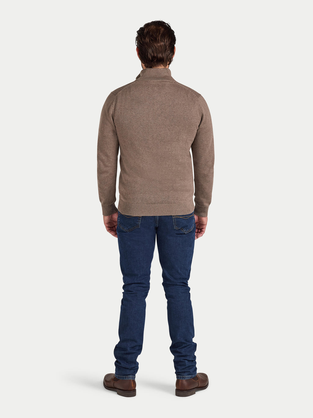 Man wearing a brown sweater and blue jeans on a white background
