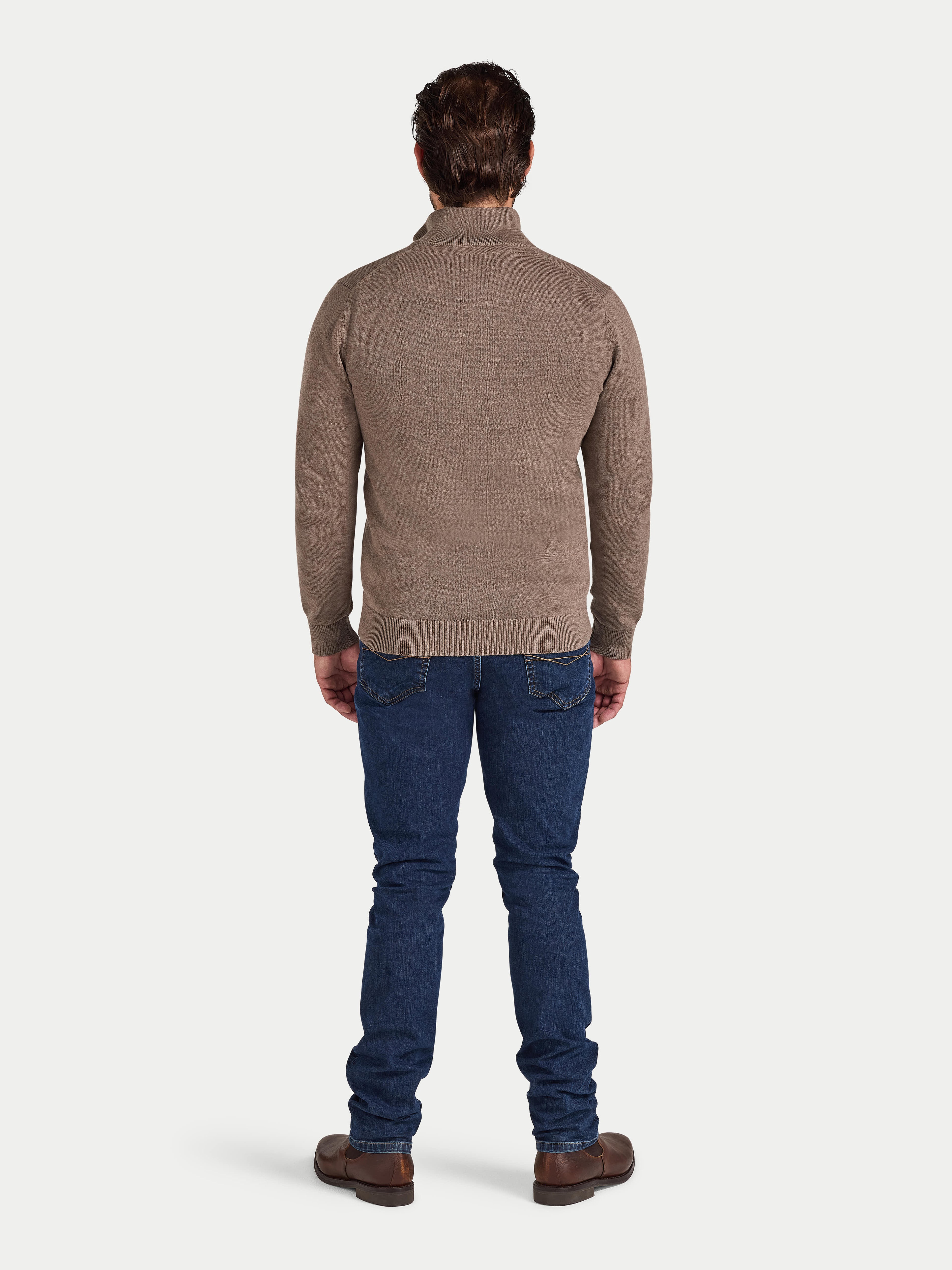 Man wearing a brown sweater and blue jeans on a white background