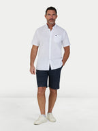 Man wearing a white short-sleeve shirt and navy shorts on a white background