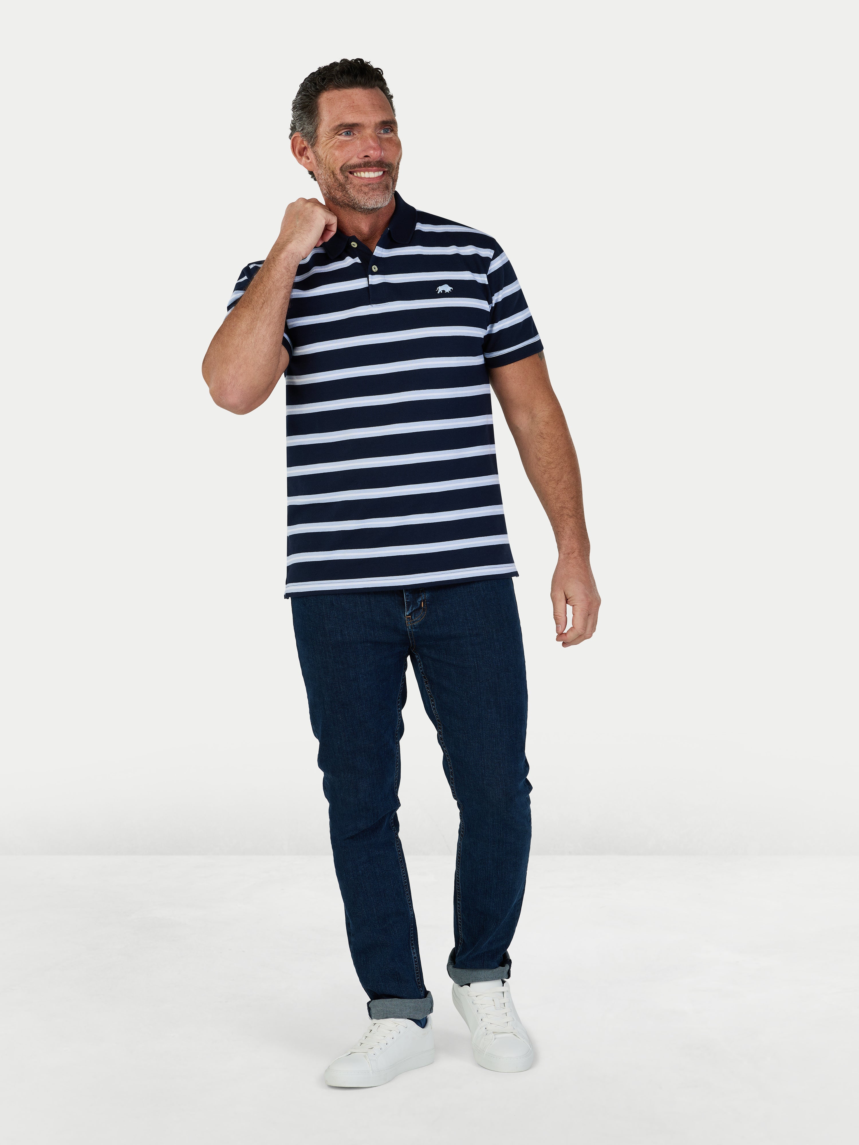 Man wearing a navy and white striped polo shirt and dark jeans on a white background