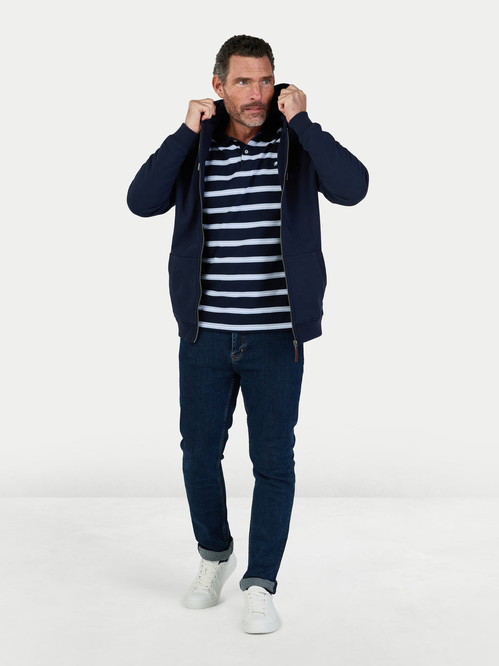 Man wearing a navy jacket, striped shirt, and jeans on a white background