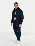 Man wearing a navy blue jacket, striped shirt, and jeans on a white background