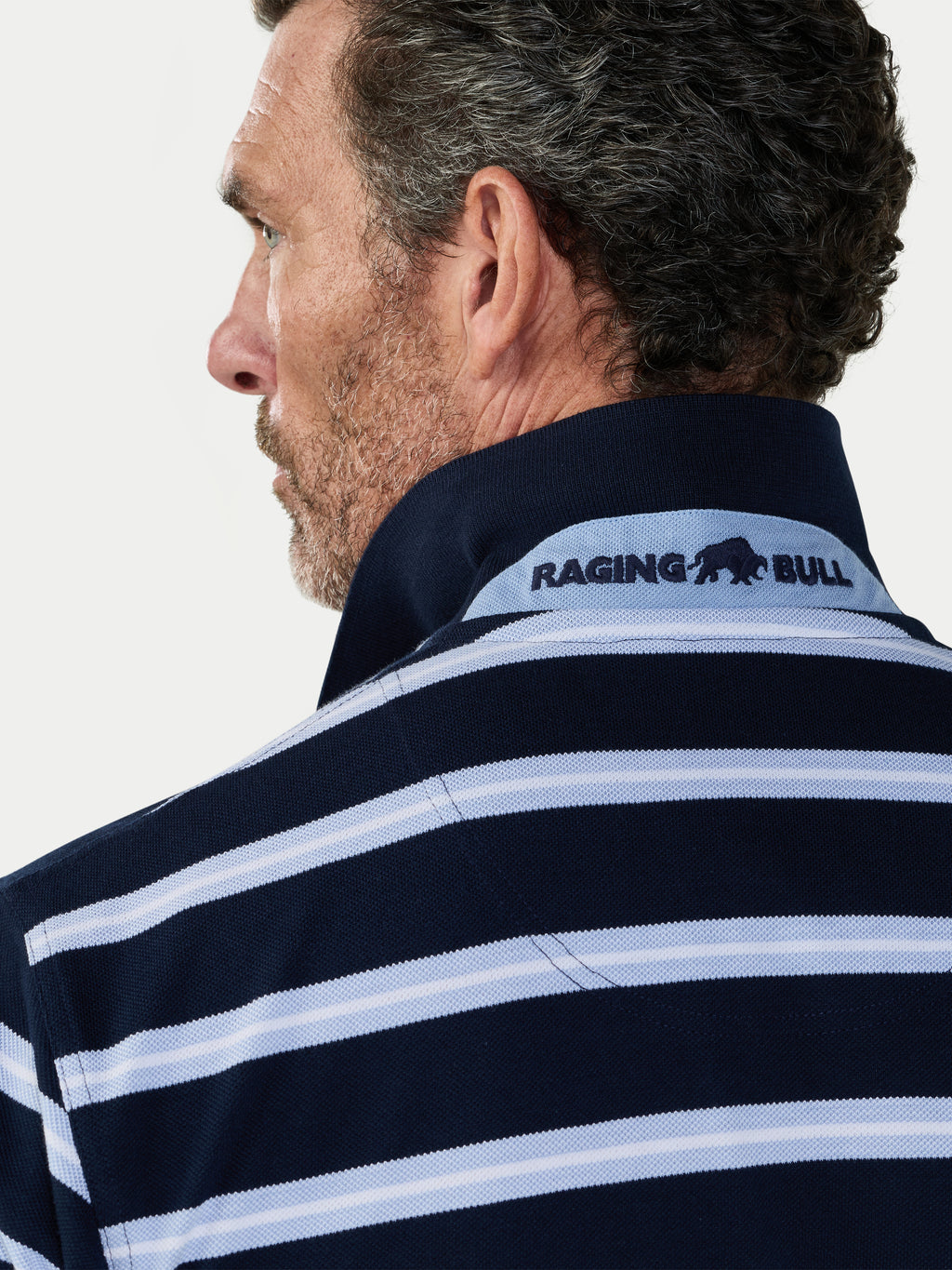 Man wearing a navy and white striped shirt with 'Raging Bull' logo on a light gray background