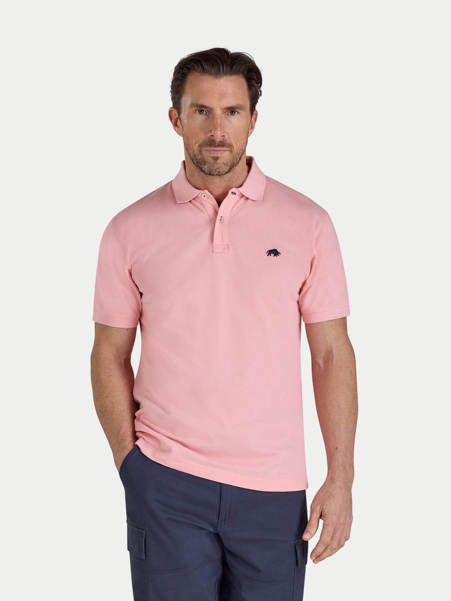 Man wearing a pink polo shirt with a small logo on a white background
