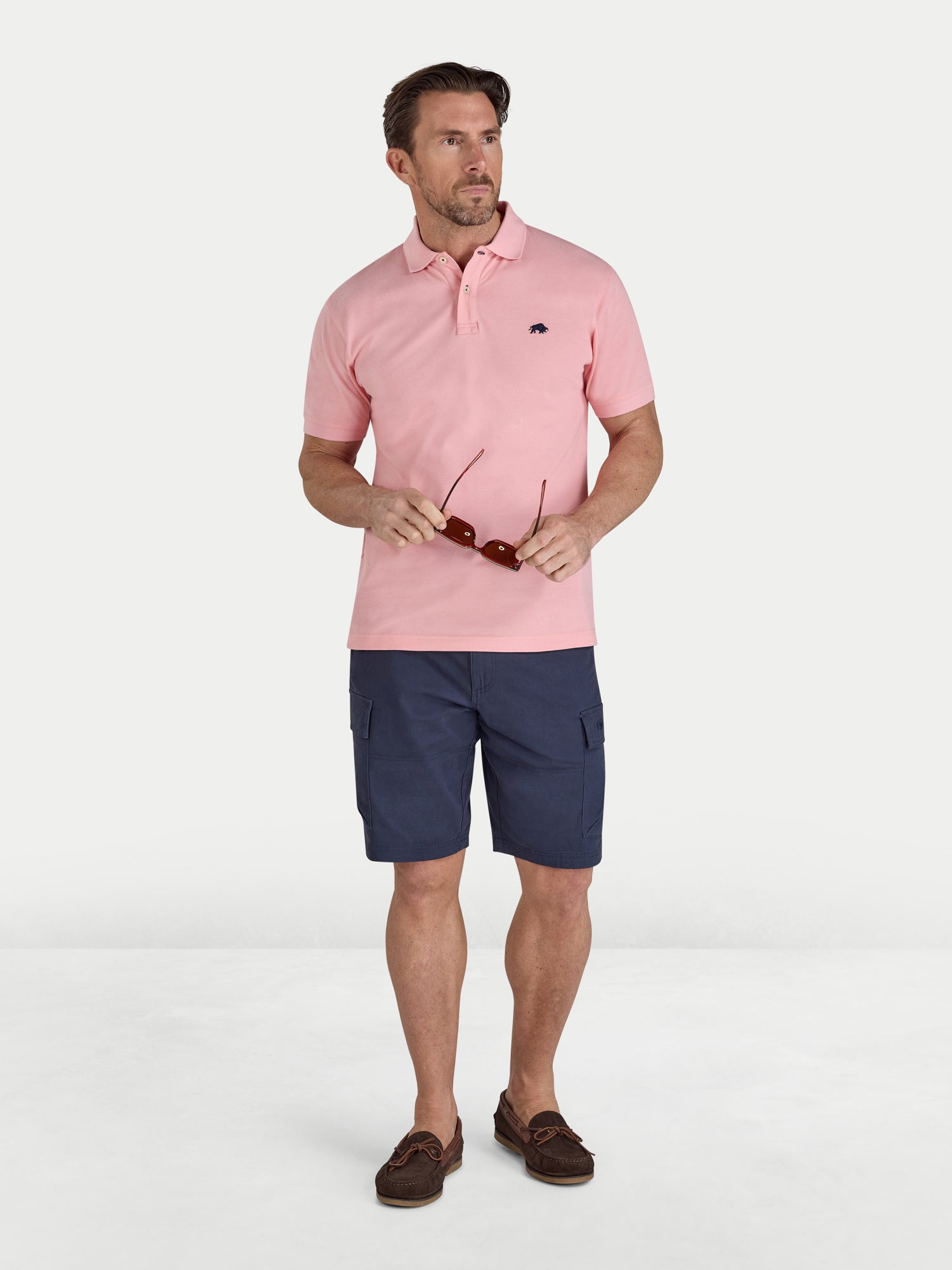 Man wearing a pink polo shirt and navy shorts on a white background