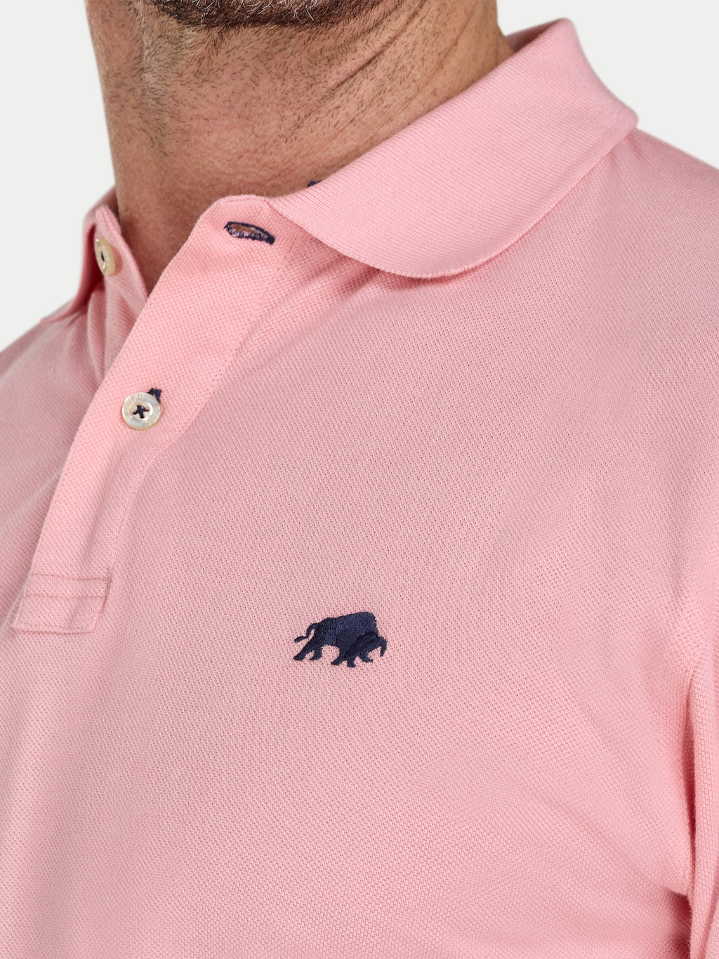 Close-up of a pink polo shirt with a small logo on a white background