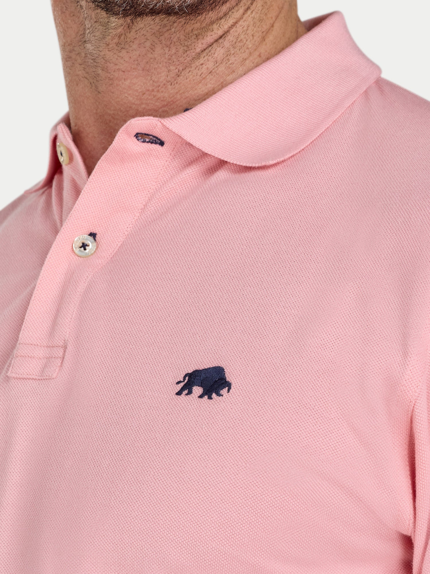 Close-up of a pink polo shirt with a small logo on a white background