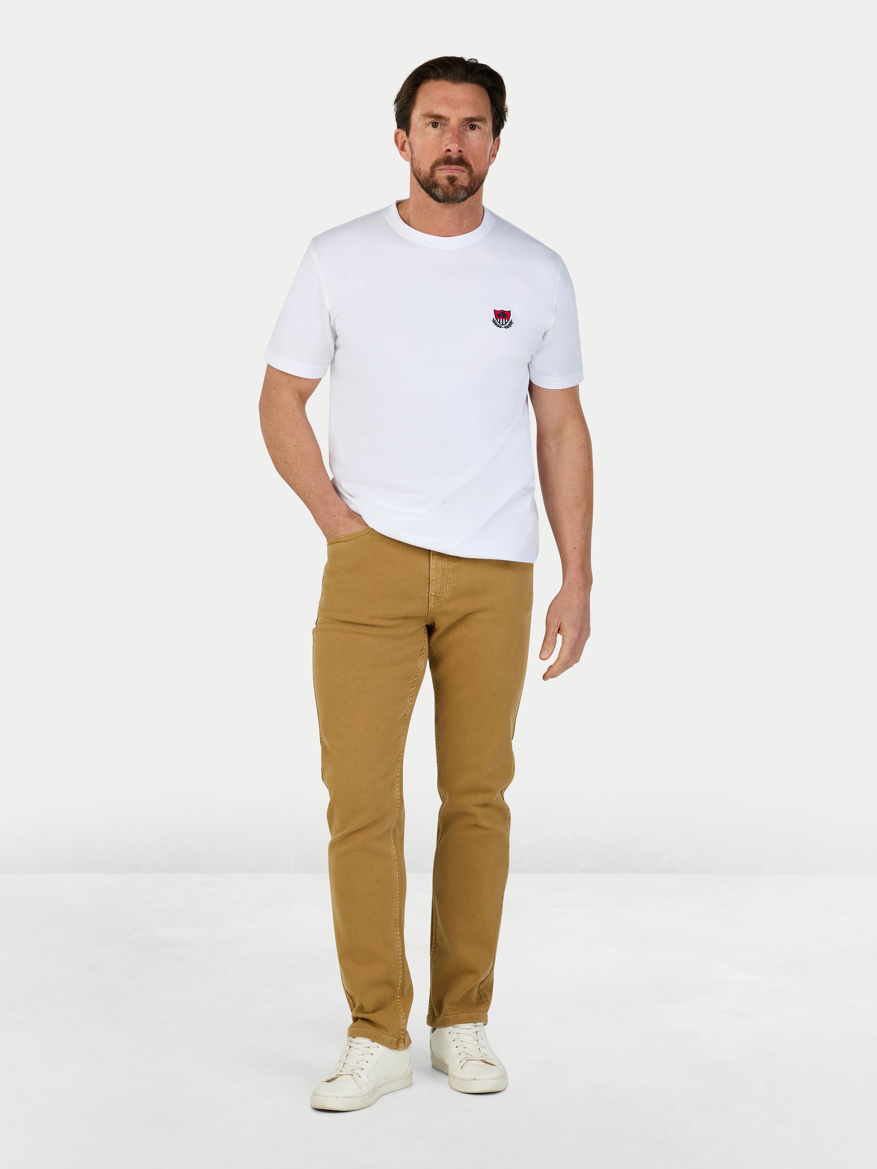 Man wearing a white t-shirt with a logo and beige pants on a white background