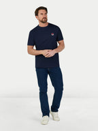 Man wearing a navy t-shirt with a logo and dark jeans on a white background