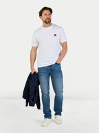 Man wearing a white t-shirt, blue jeans, and white sneakers holding a dark jacket on a light gray background