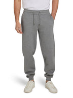 A man wearing light grey cuffed sweatpants with a drawstring waist, standing with hands in pockets and white sneakers on feet.