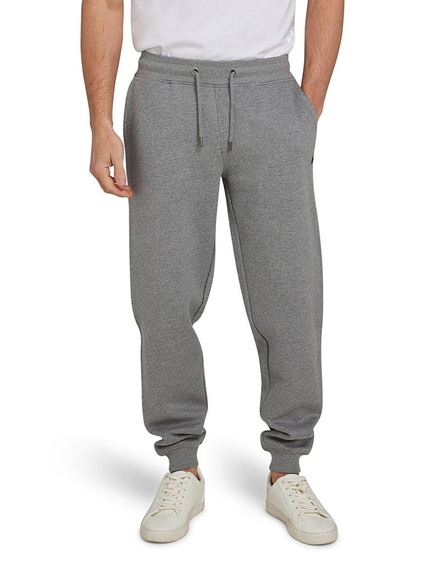 A man wearing light grey cuffed sweatpants with a drawstring waist, standing with hands in pockets and white sneakers on feet.