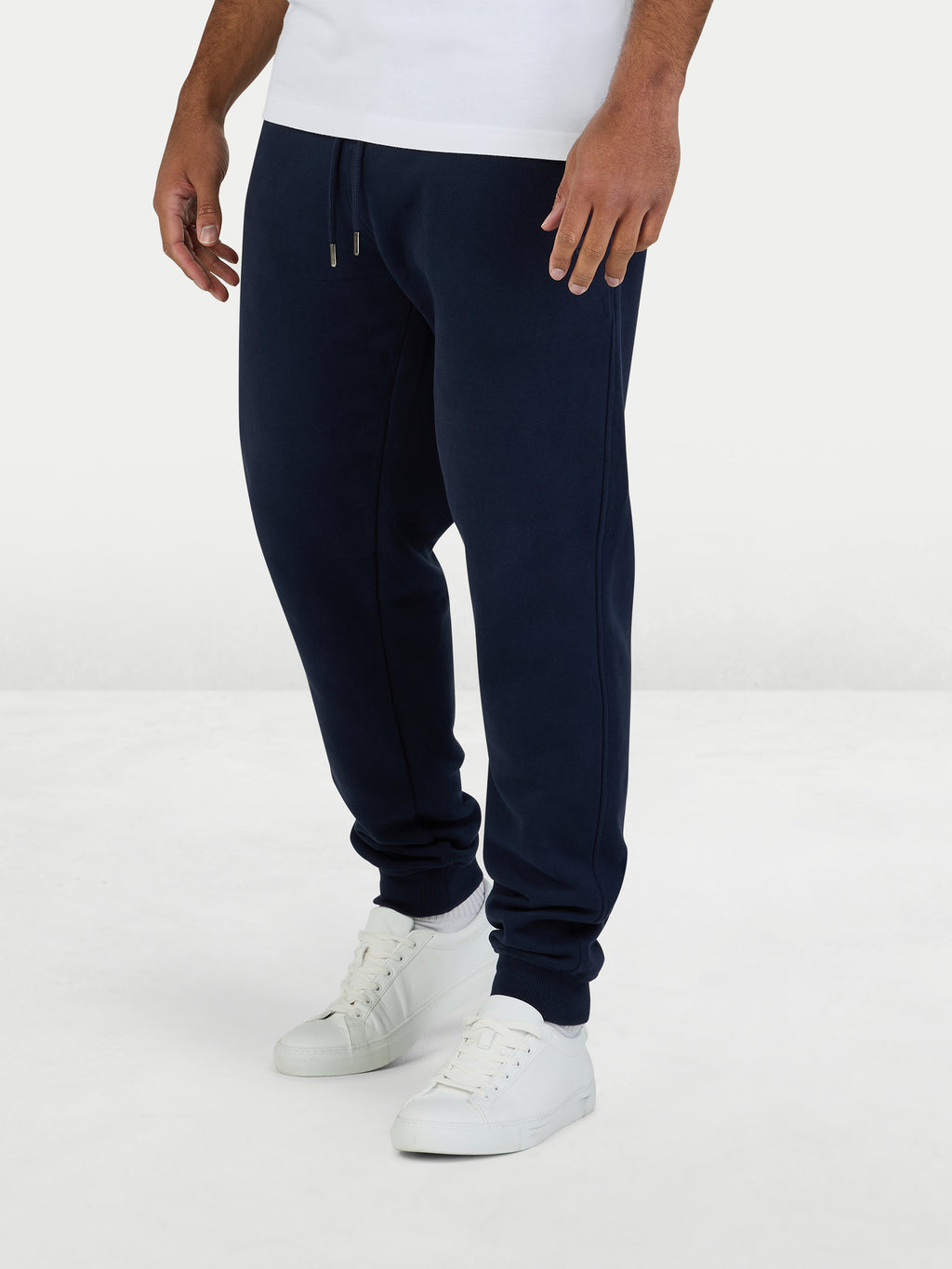 Person wearing navy jogger pants and white sneakers on a white background