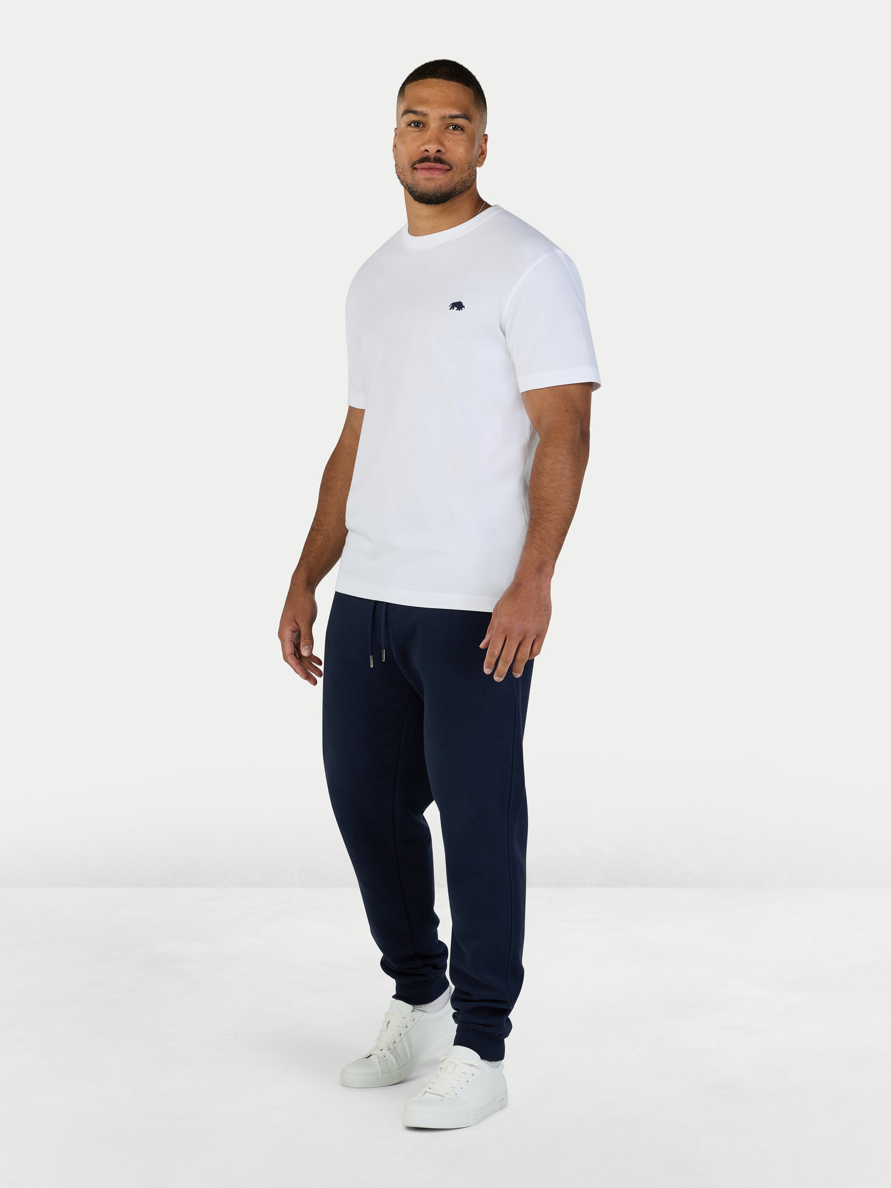 Man wearing a white t-shirt and navy jogger pants on a white background