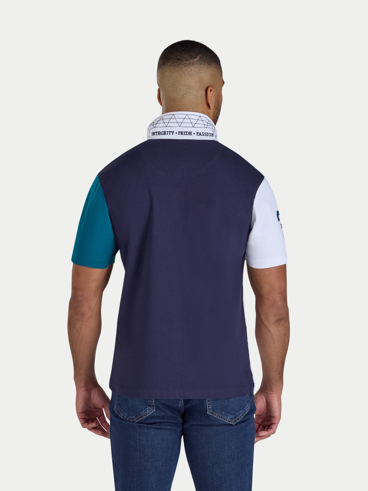 Man wearing a navy polo shirt with teal sleeves and a white collar, standing against a light gray background.