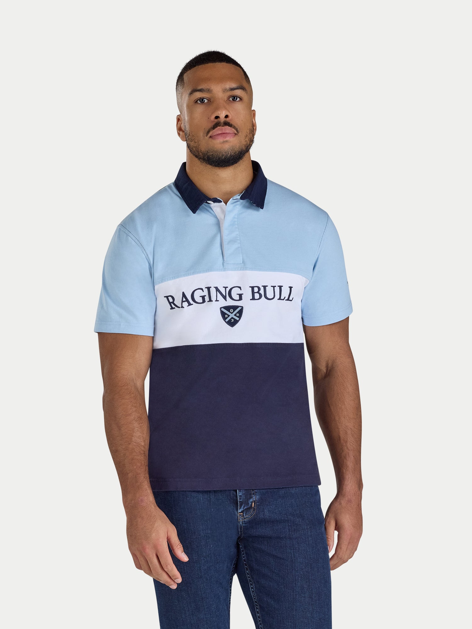 Man wearing a light blue and navy polo shirt with 'Raging Bull' logo on a white background