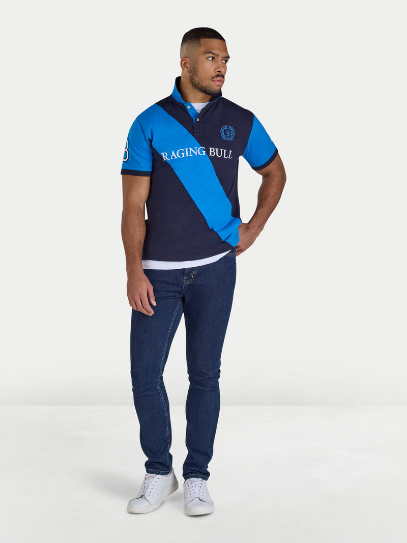 Man wearing a blue and navy polo shirt with 'Raging Bull' branding on a white background