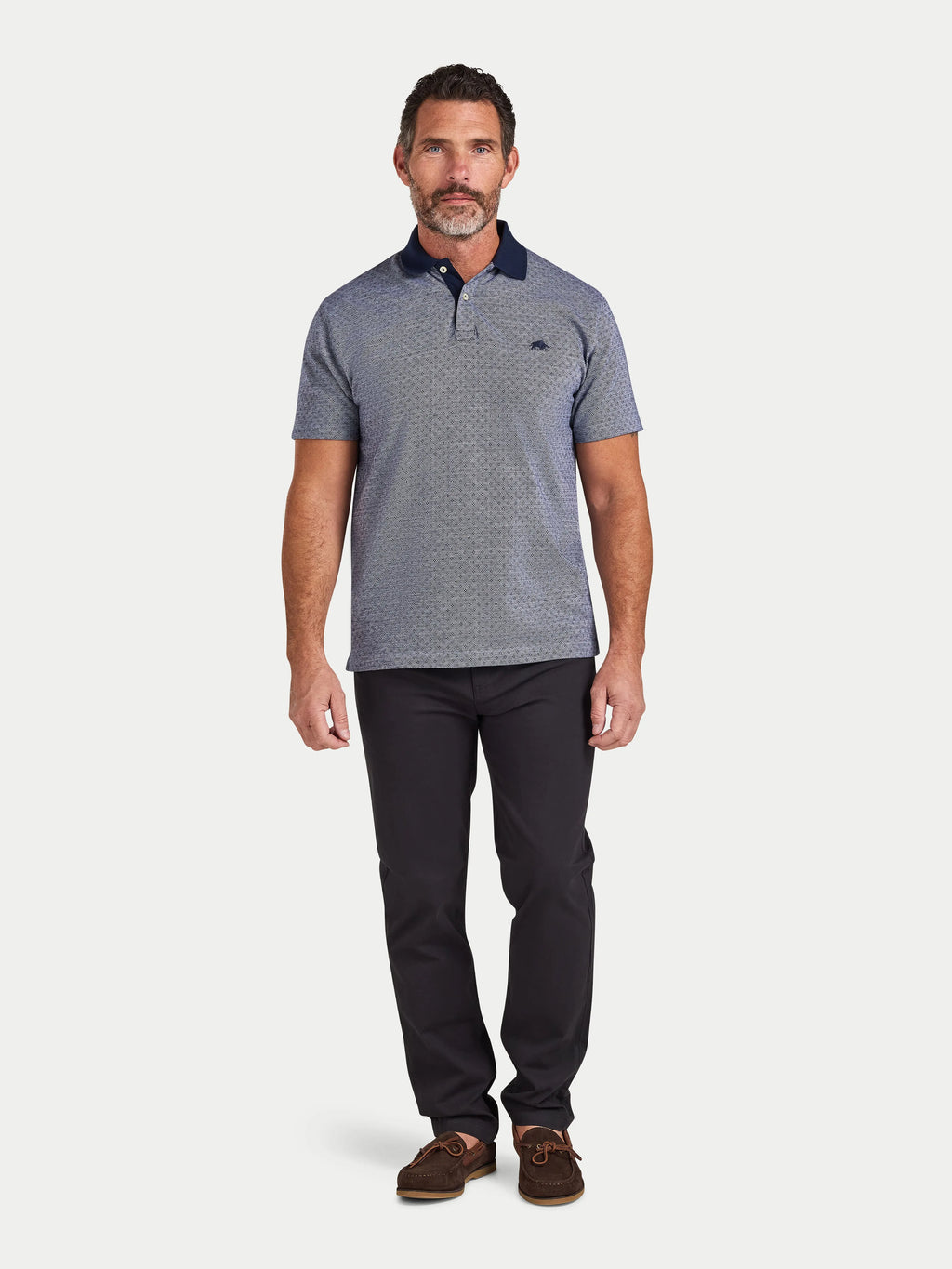 Man wearing a gray patterned polo shirt and black pants on a white background