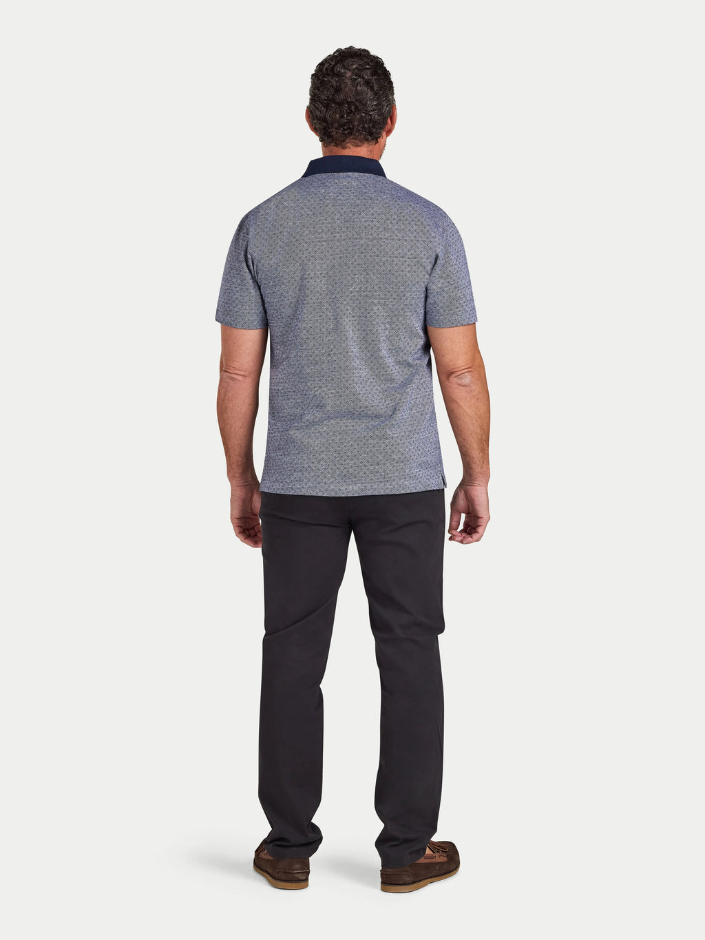 Man wearing a patterned polo shirt and dark pants on a white background