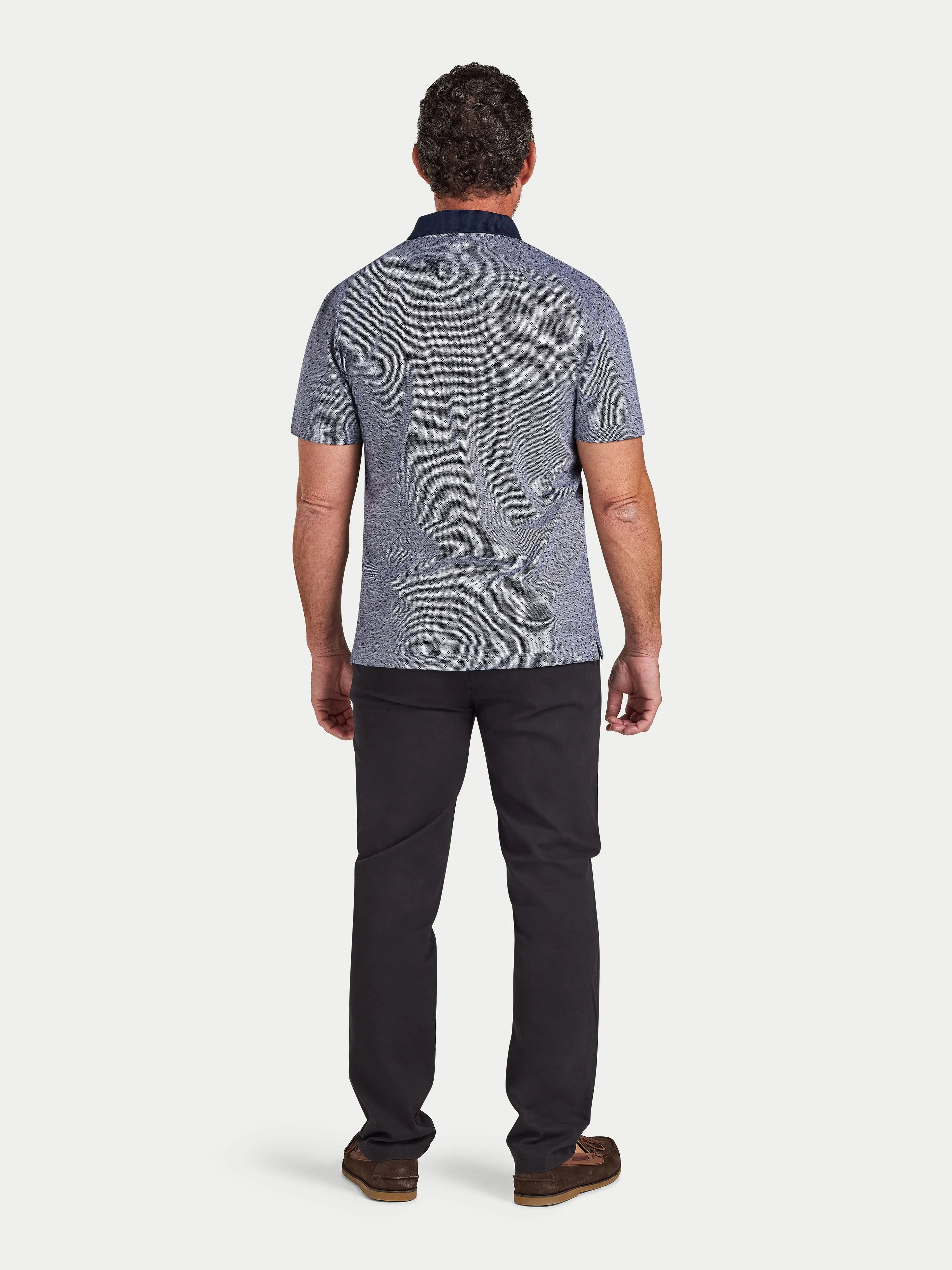 Man wearing a patterned polo shirt and dark pants on a white background
