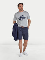 Man wearing a gray t-shirt with a logo and navy shorts on a white background