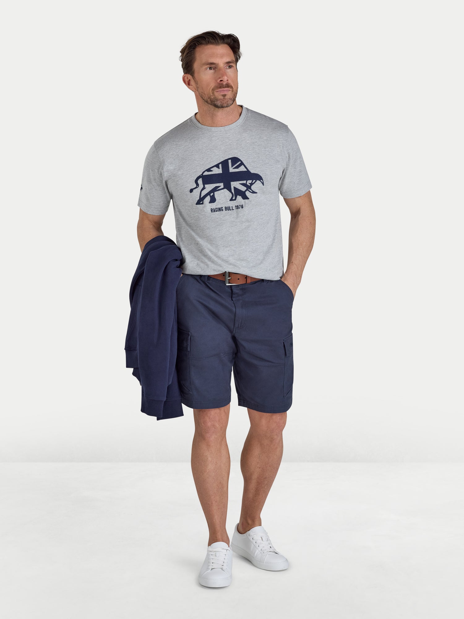 Man wearing a gray t-shirt with a logo and navy shorts on a white background