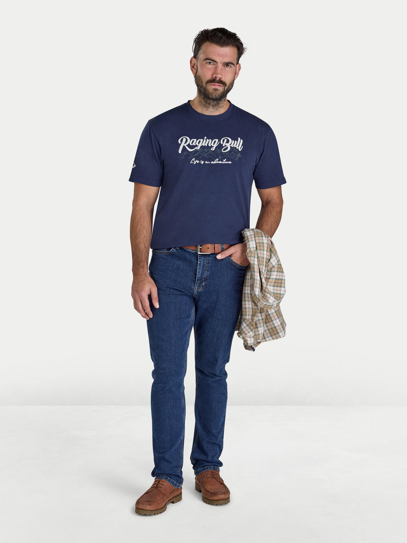 Man wearing a navy blue t-shirt with 'Raging Bull' logo and blue jeans on a white background