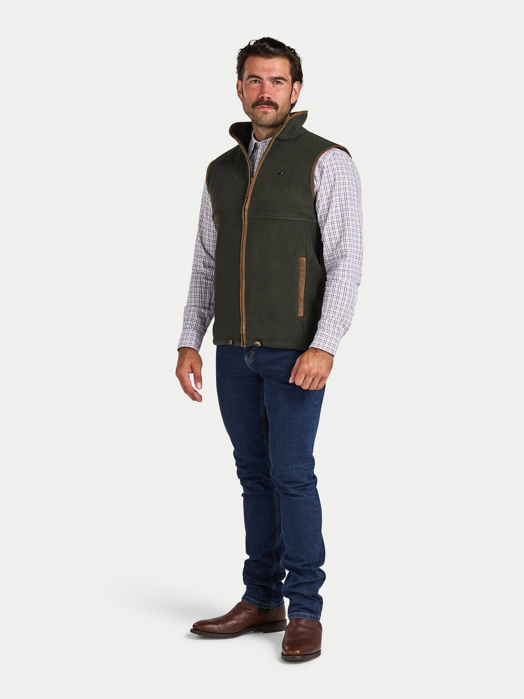 Man wearing a green vest over a plaid shirt with blue jeans on a white background